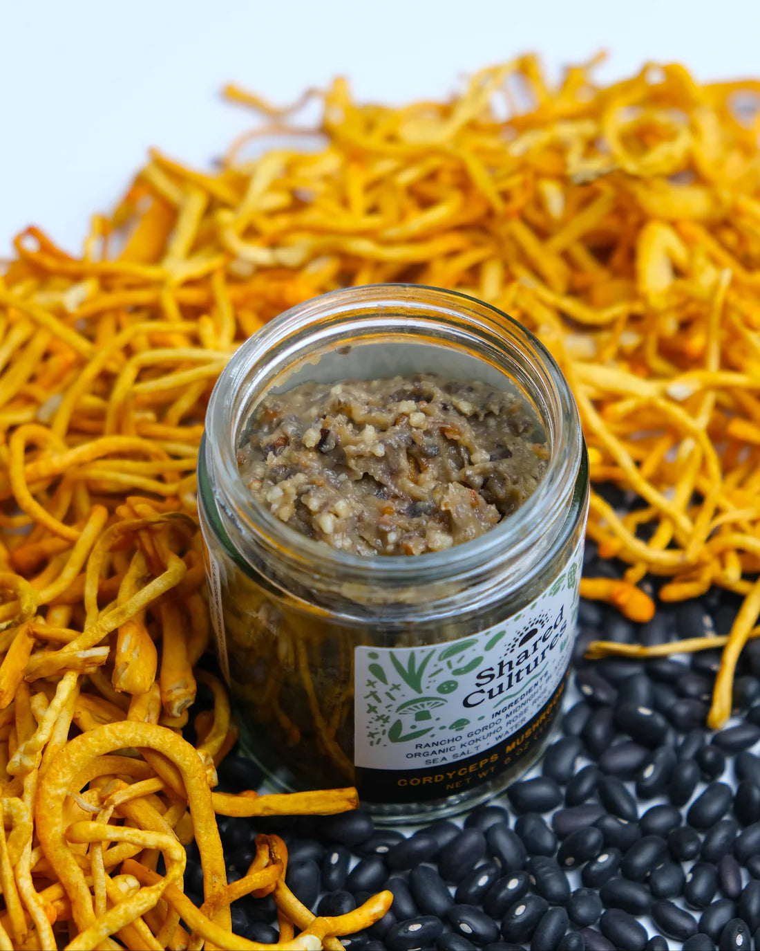 Jar of spreadable food with yellow noodles and black beans on a white background