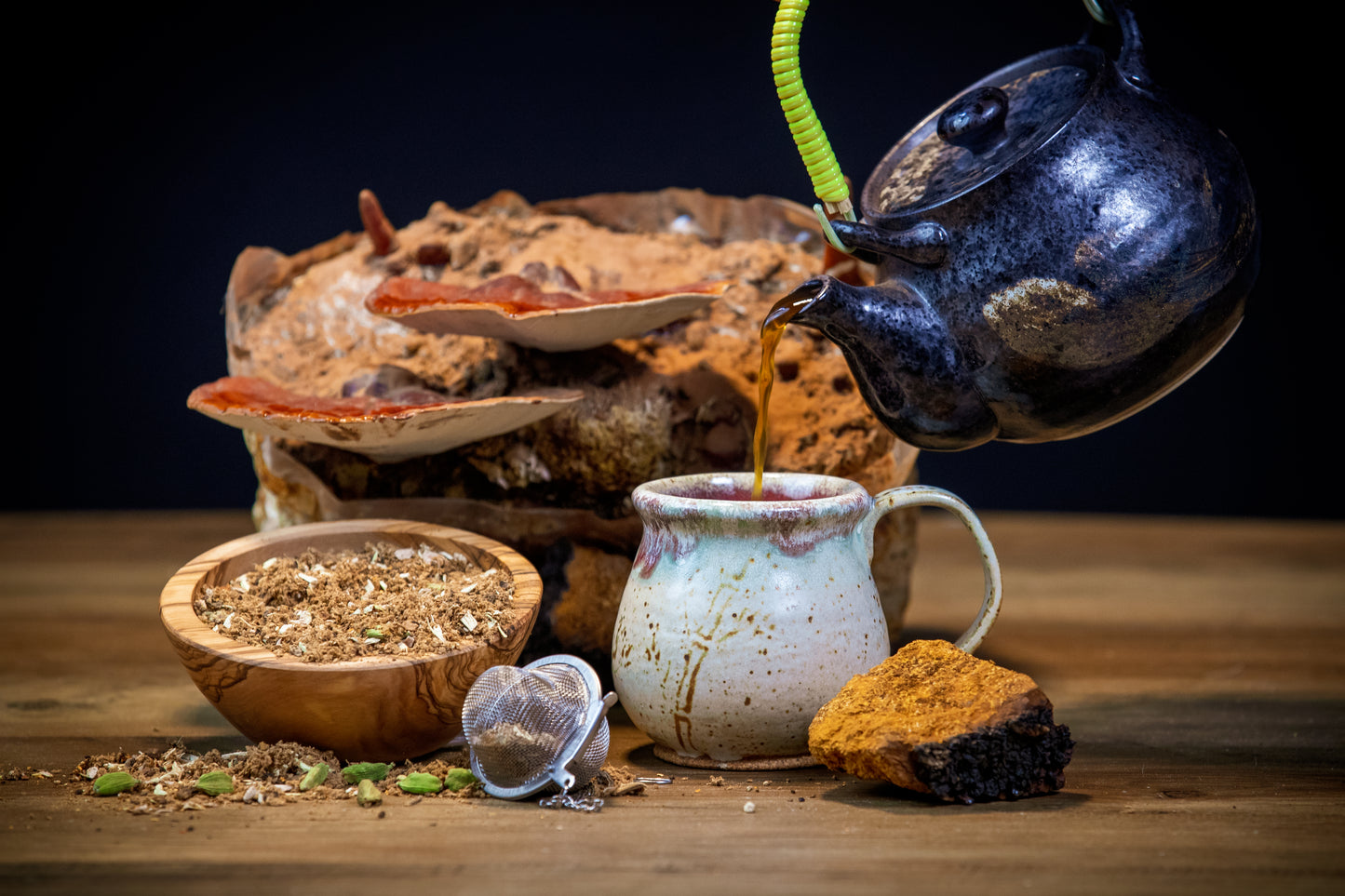 Tea being poured from a teapot into a cup on a wooden surface with tea leaves and a teacup in the background.