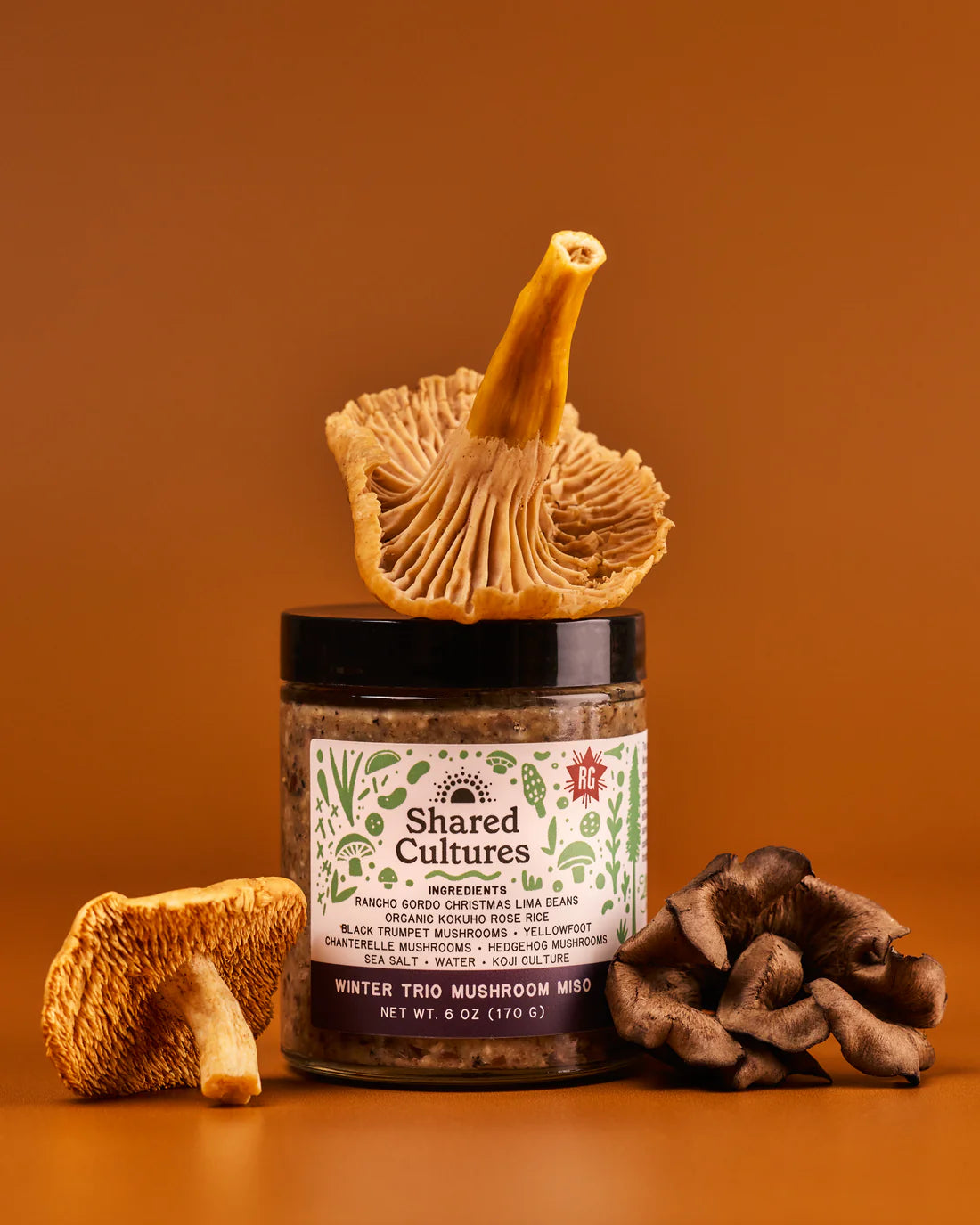 Jar of 'Shared Cultures' mushroom mist with mushrooms on an orange background